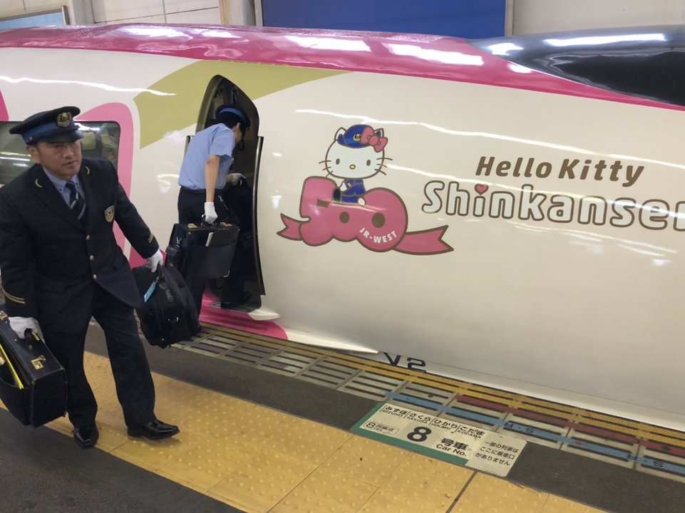 Conducteurs de train se tenant près d'un train Shinkansen à thème Hello Kitty.