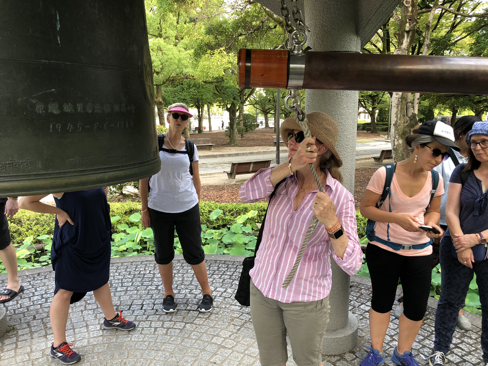 Des touristes qui sonnent une grande cloche dans un jardin.