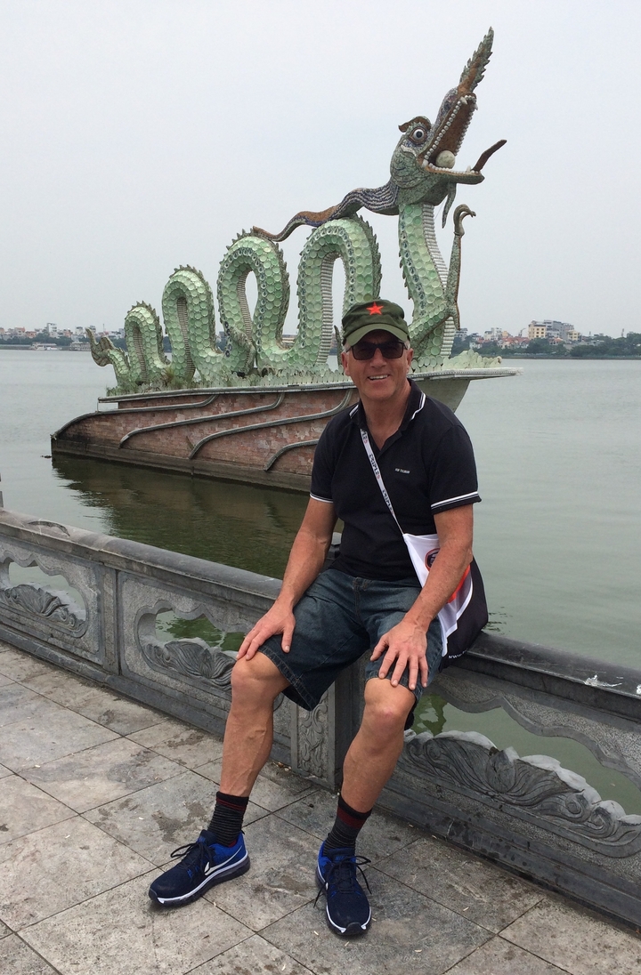 Homme assis près d'un lac avec une sculpture de dragon en arrière-plan.
