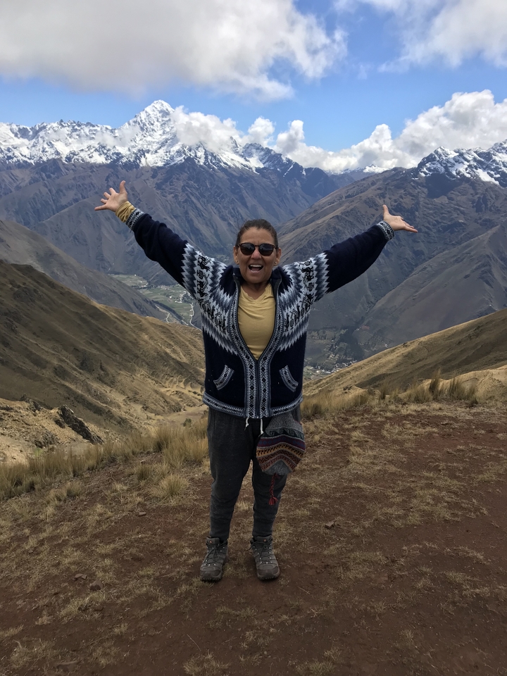 Femme heureuse aux bras étendus devant un paysage montagneux.