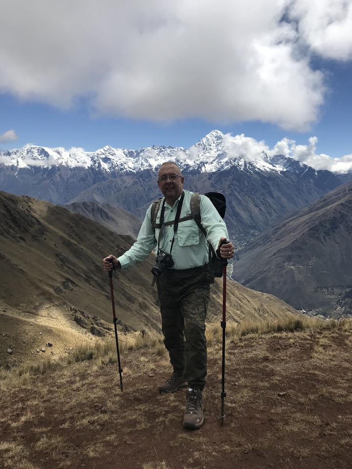 Homme avec bâtons de randonnée posant devant des montagnes enneigées.