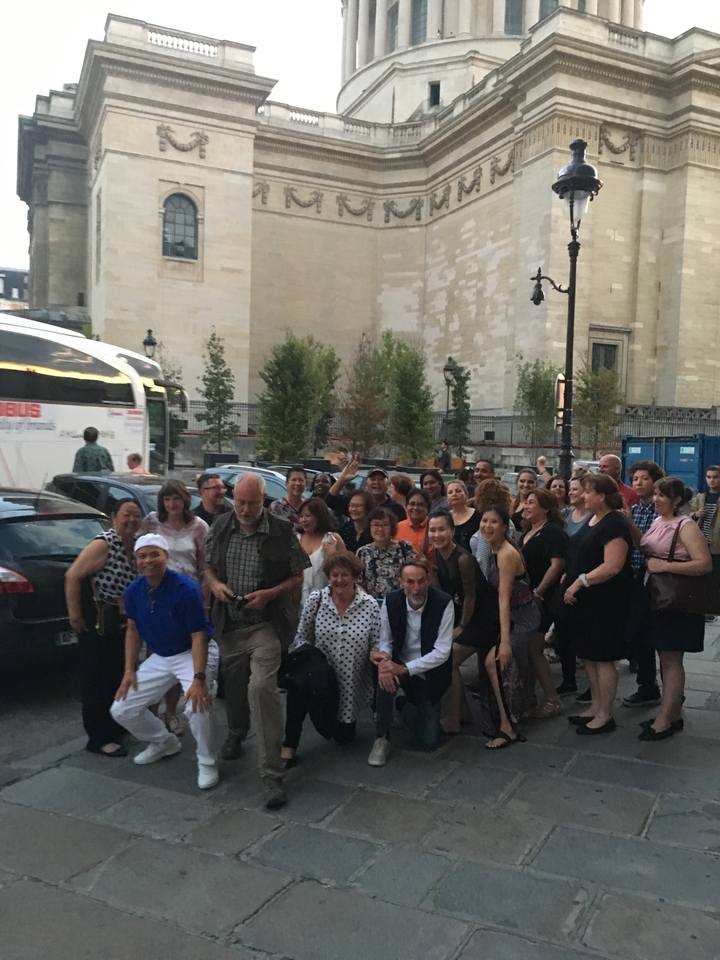 Un grand groupe de personnes posant à l'extérieur près d'un mur avec des arbres en arrière-plan.