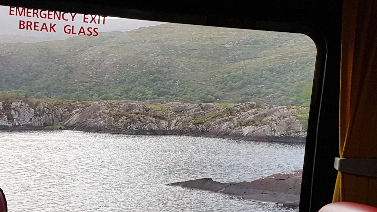 Vue d'un lac et de montagnes depuis l'intérieur d'un bus.