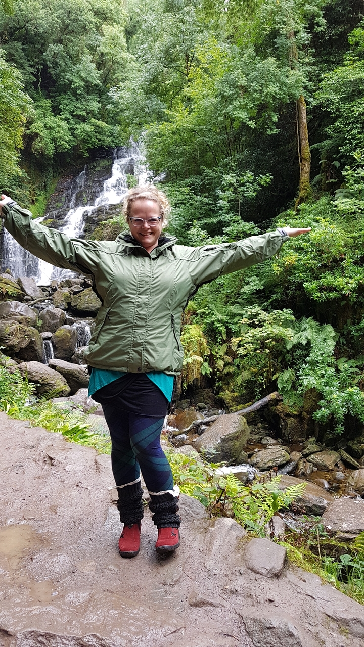 Person posing with arms outstretched by a waterfall.