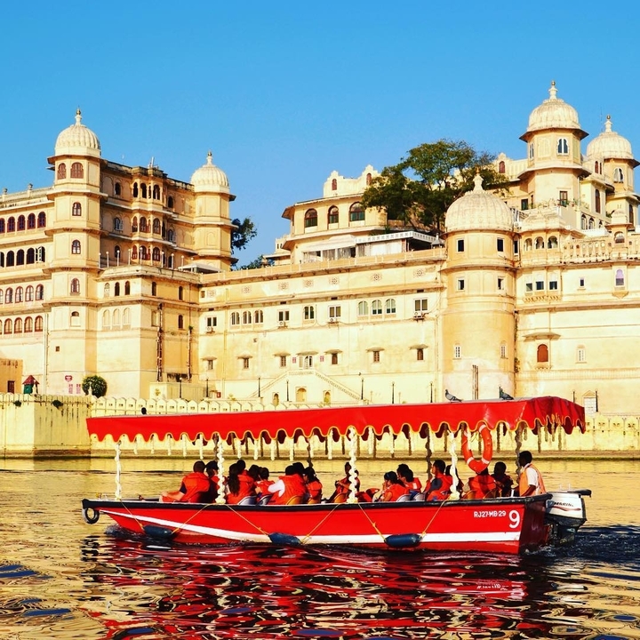 Tour boat with passengers in red life jackets glides before a grand palace façade.