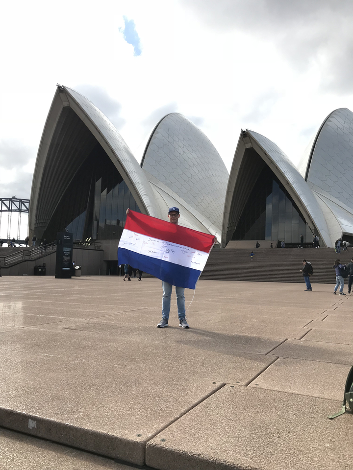 Person holding a flag in front of a famous opera house.