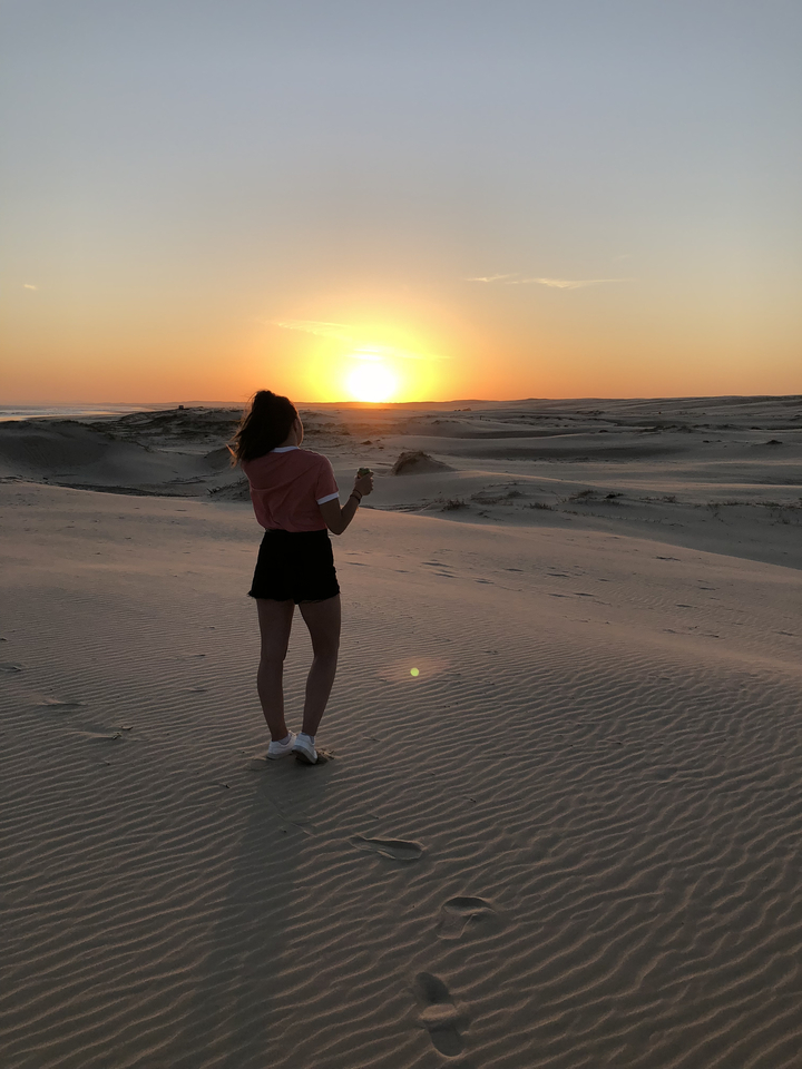 Person standing on sand dunes with a sunset.