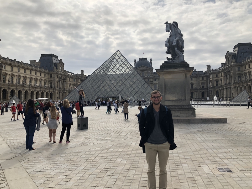 Homme posant devant la Pyramide du Louvre.
