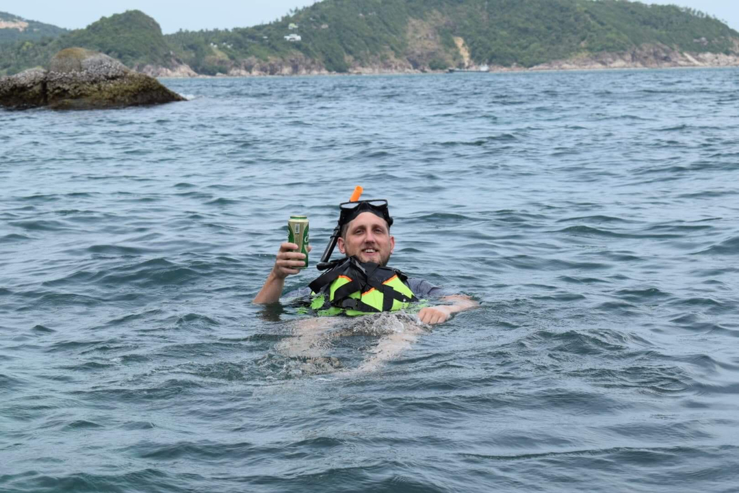 Une personne nageant dans la mer tout en tenant une boisson, portant un masque de plongée et un gilet de sauvetage.