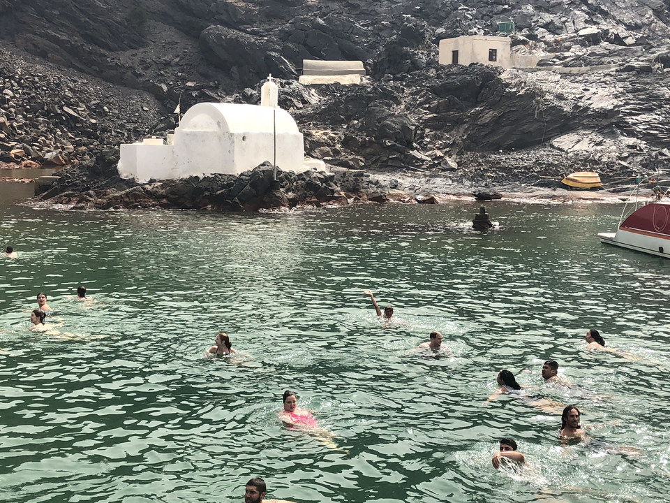 People swimming near a chapel on rocky shores.