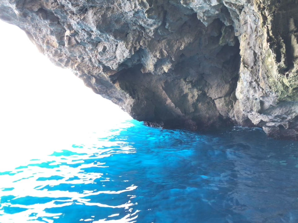 Ouverture de grotte avec un soleil éclatant au-dessus d'une eau turquoise.