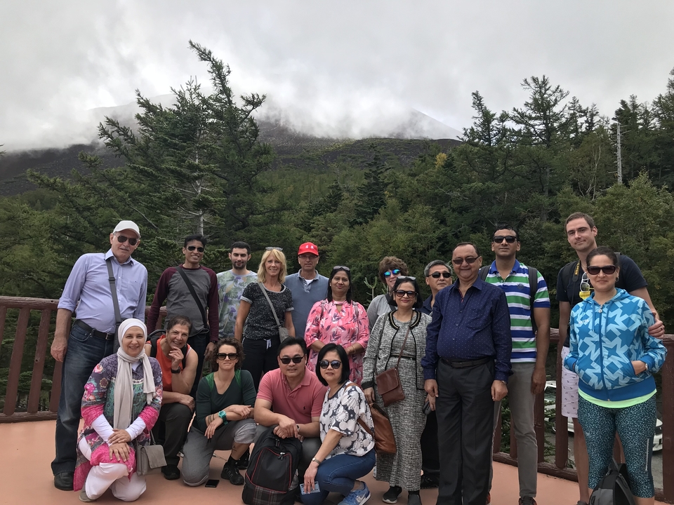 Grand groupe posant devant des arbres et un sommet de montagne.