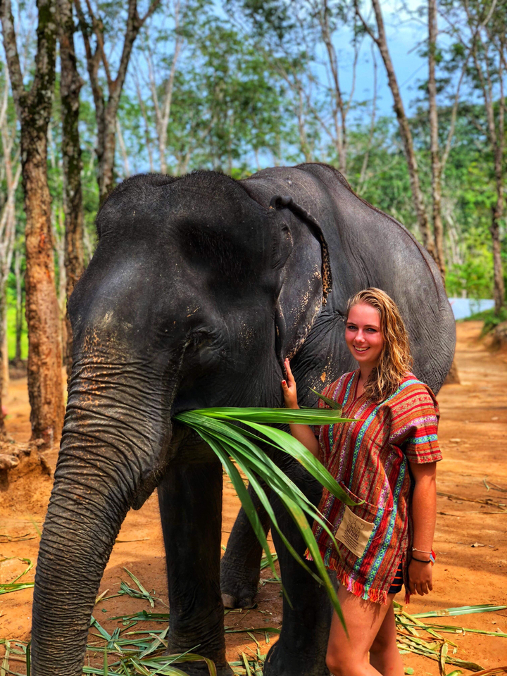 Woman smiling while standing next to an elephant.