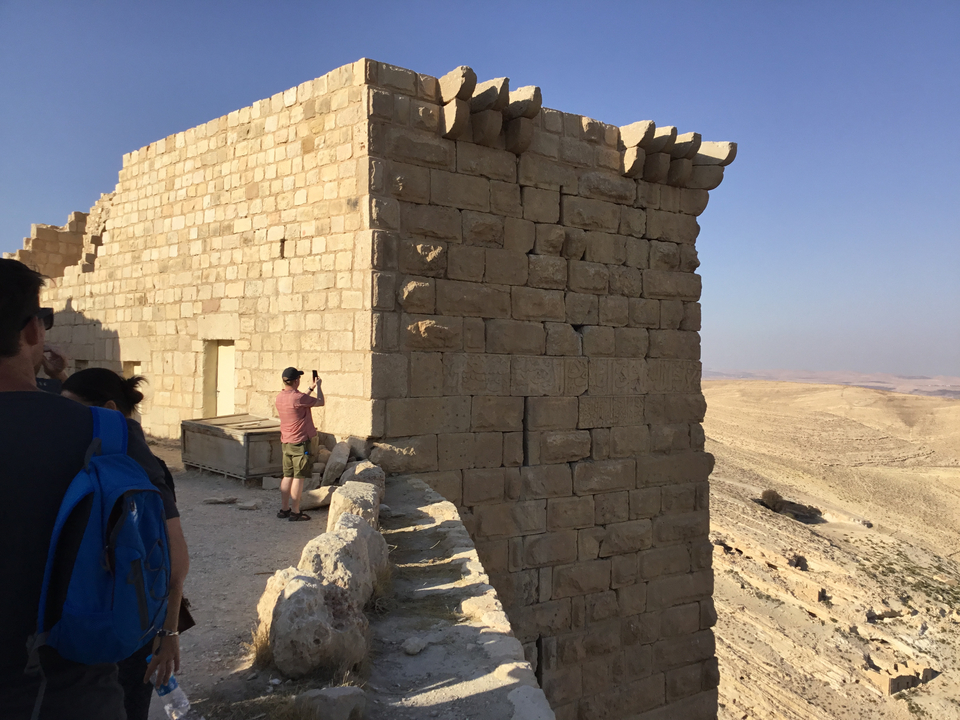 Bâtiment en pierre sur une colline avec une personne prenant une photo.