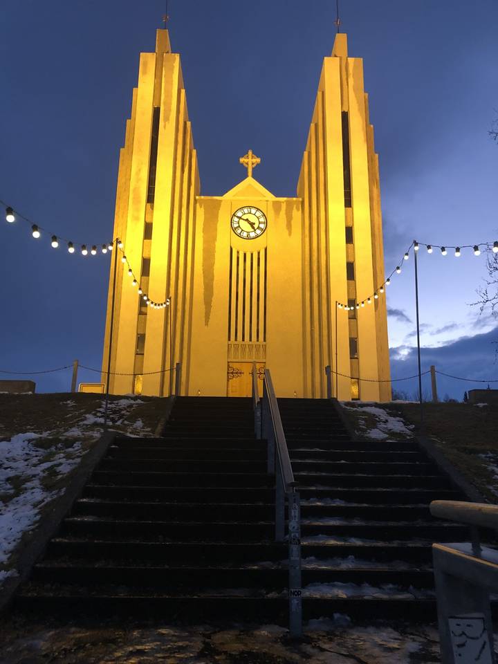 Un bâtiment jaune avec une horloge et des lumières la nuit.