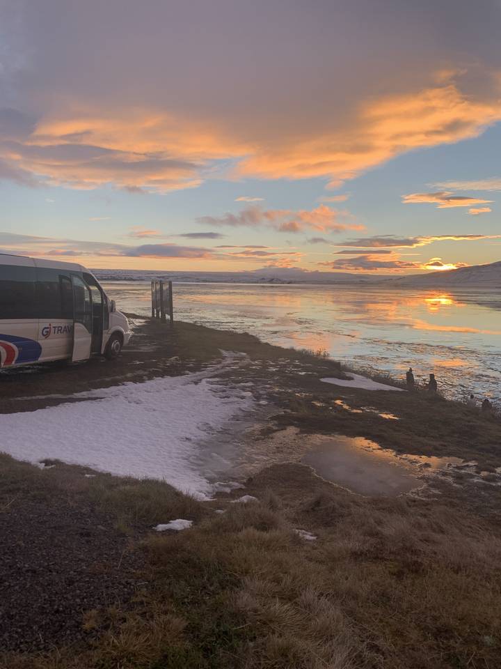 Vue du coucher de soleil sur un paysage enneigé et rocheux avec une voiture garée.