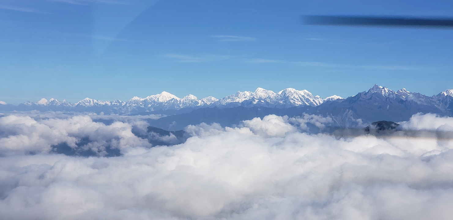 Snow-capped Himalayan peaks rise above a sea of clouds under a crisp blue sky.