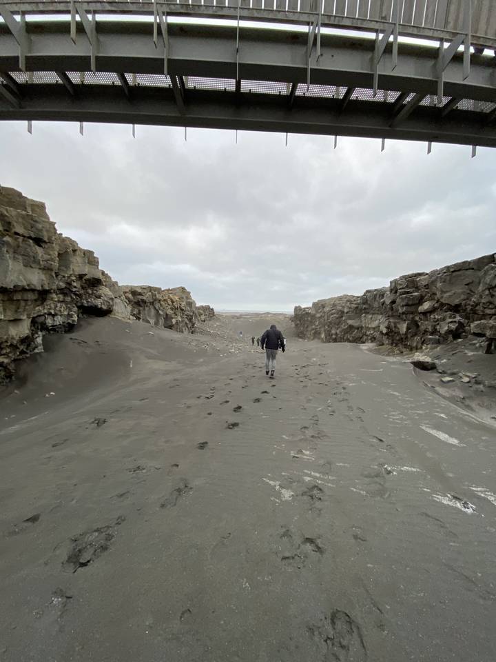 Person walking on a rocky beach under a bridge.
