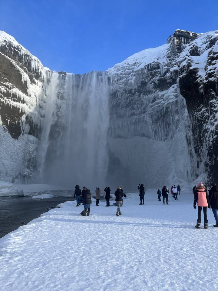 Waterfall with people standing nearby in a snowy environment.