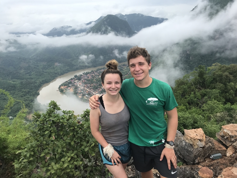 Two people posing on a hill with a river and village below.