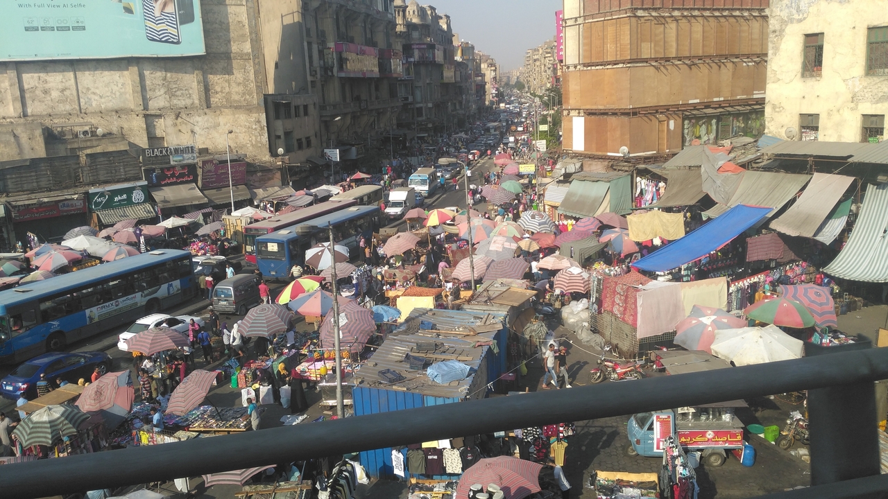 Scène de marché en plein air animé dans une ville avec des parasols colorés et des étals.