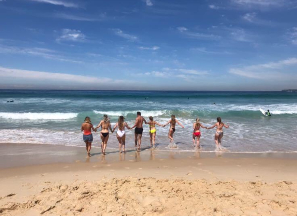 Group holding hands walking into the ocean waves.