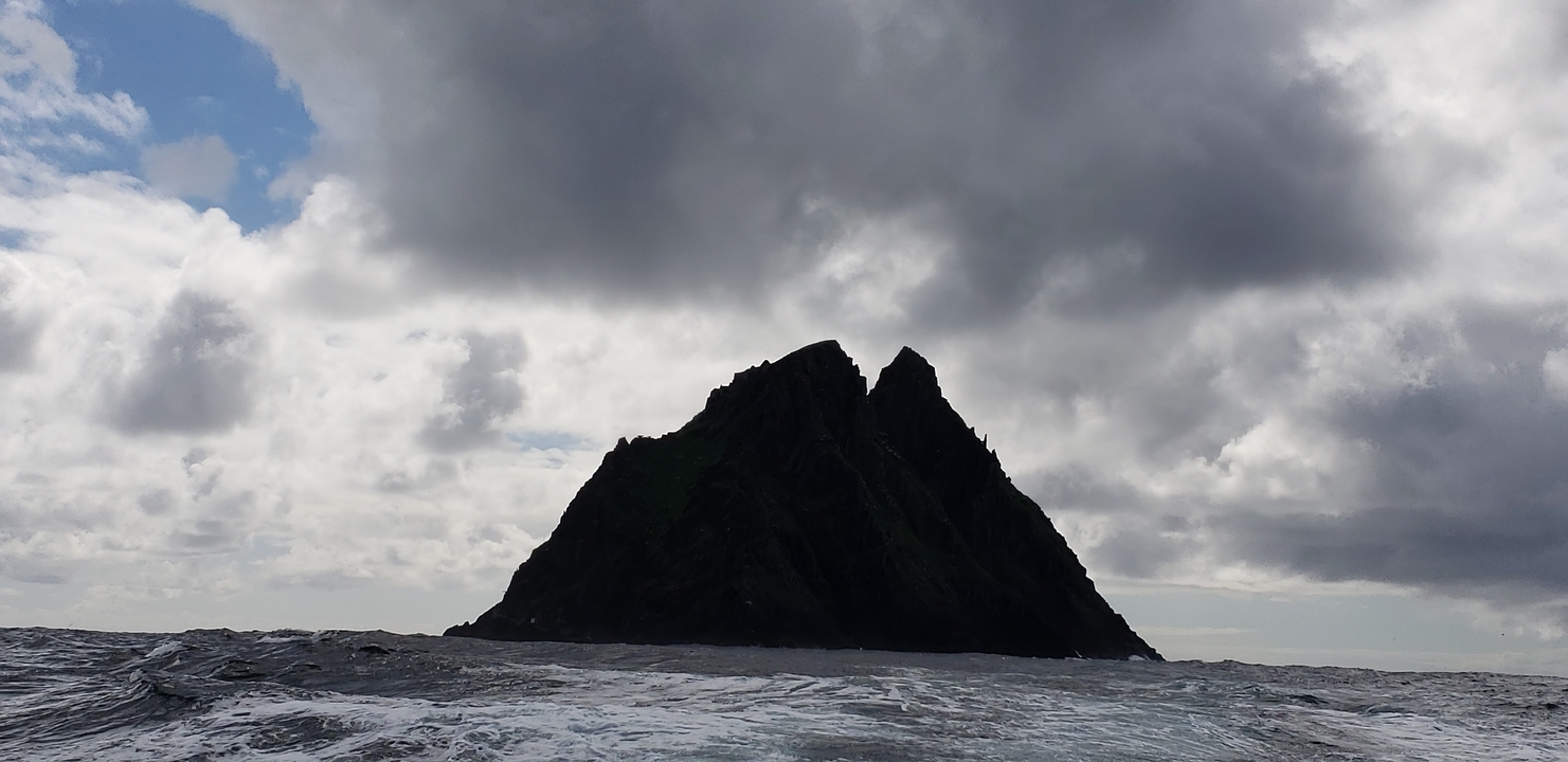 Îlot rocheux silhouetté contre un ciel nuageux.
