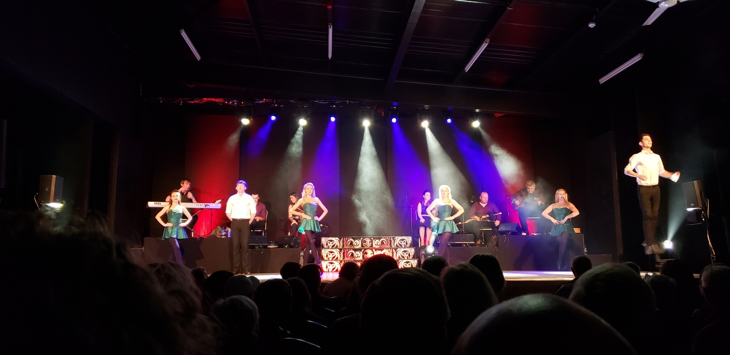 Spectacle sur scène avec danseurs et musiciens sous des éclairages vibrants.