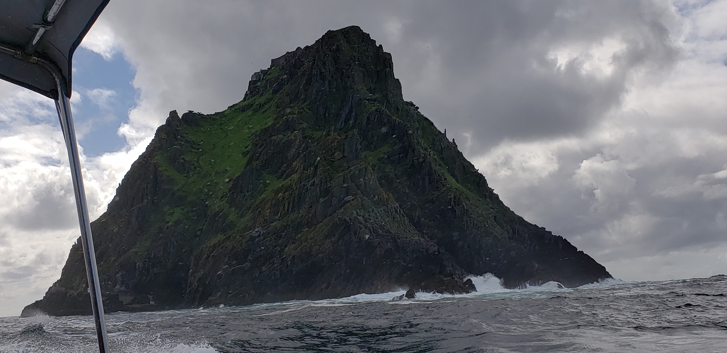 Formation rocheuse verte escarpée et accidentée entourée par la mer.