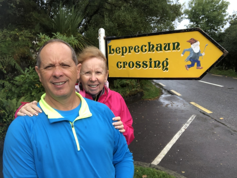 Couple posant à côté d'un panneau « Passage de lutins » sur une route rurale.