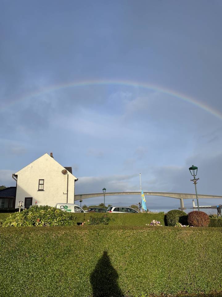 Arc-en-ciel au-dessus d'une zone herbeuse avec une maison et un mât de drapeau.