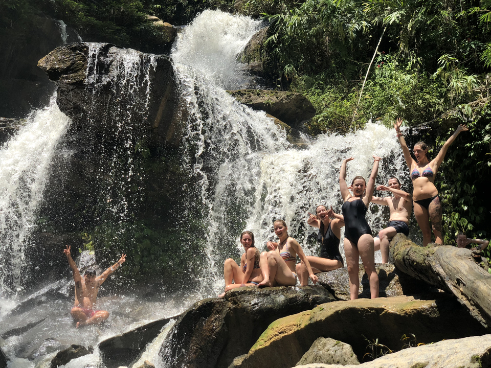 Group of people enjoying a waterfall, some posing happily.