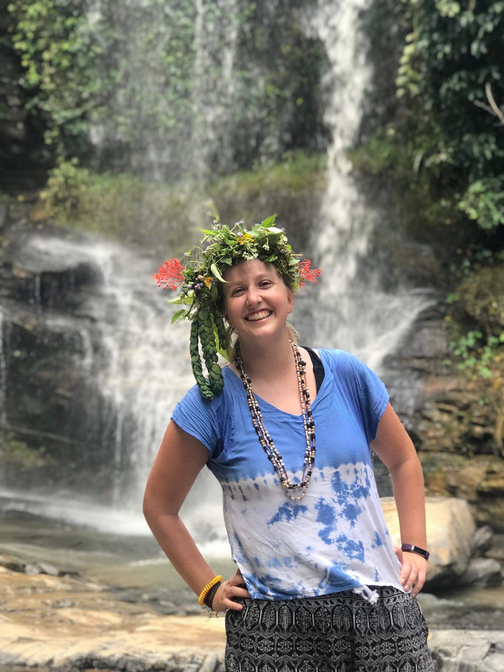 Person with a floral crown standing in front of a waterfall.