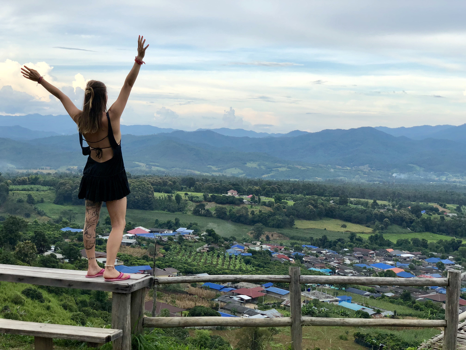 A person standing on a railing overlooking a village and mountains.