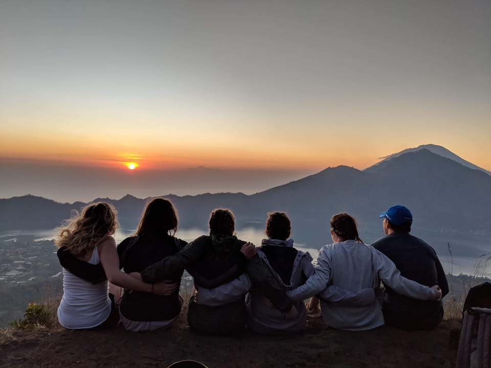 Groupe regardant un lever de soleil au-dessus des montagnes, les bras autour les uns des autres.