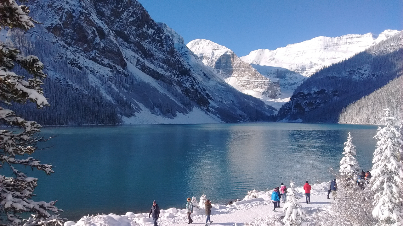 Touristen bewundern den schneebedeckten Lake Louise in einer atemberaubenden Berglandschaft.