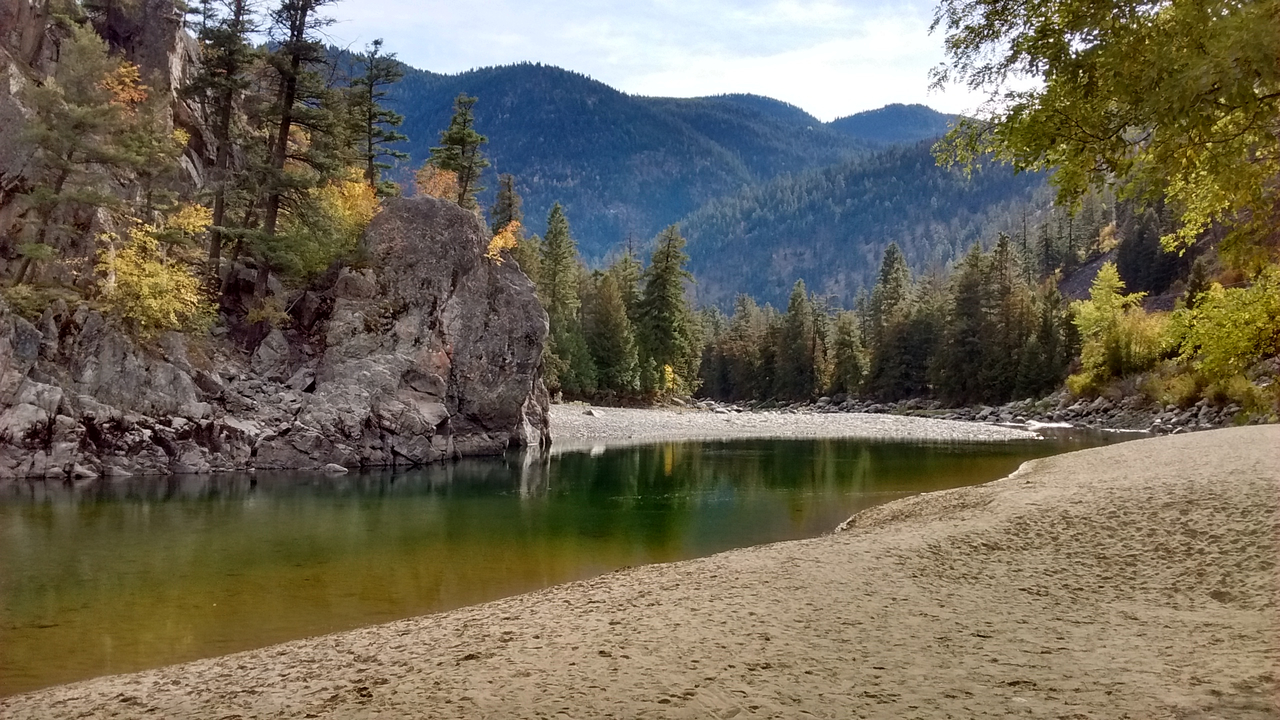 Ruhiger Felsstrand umgeben von Wald und Bergen.