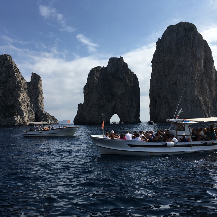 Bateaux transportant des touristes près de formations rocheuses à Capri, avec un ciel dégagé.