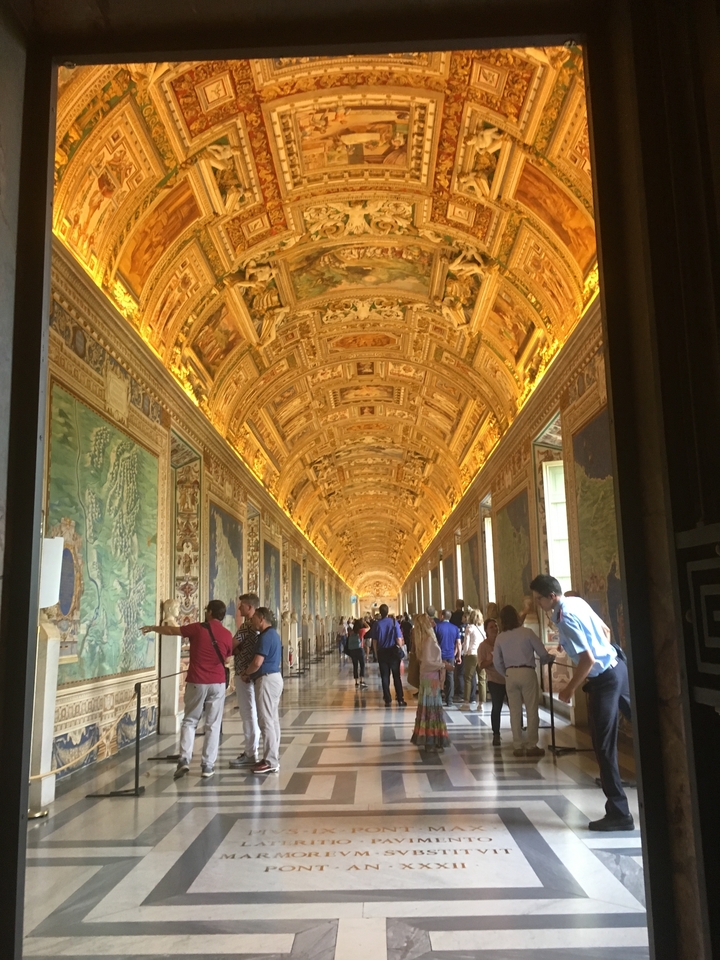Couloir avec plafonds voûtés et décorations ornées, bondé de visiteurs.