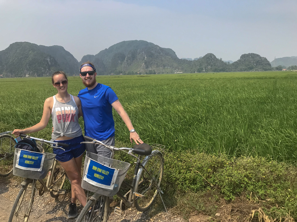 Two people with bicycles in a vast green rice field.