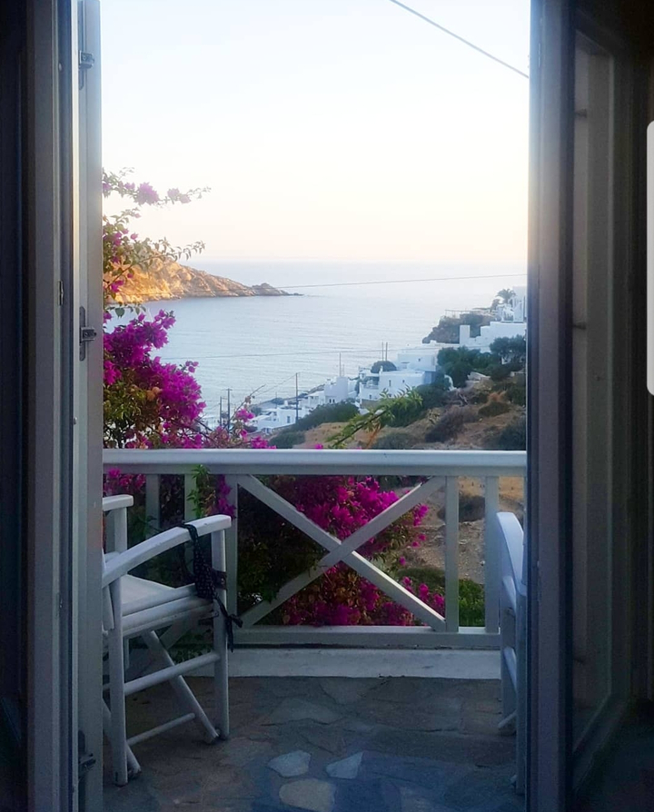 View of a coastal village with white buildings and pink flowers from a balcony.