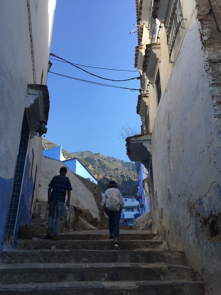 Deux personnes marchant dans une ville de montagne aux murs distinctifs peints en bleu.
