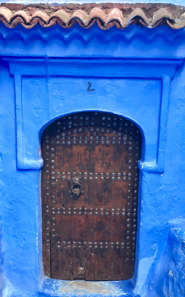 Porte décorative bleue avec clous métalliques dans une façade colorée.
