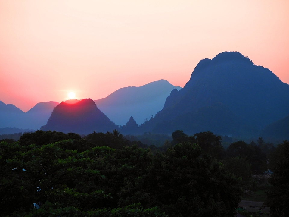 Magnifique coucher de soleil sur des collines ondulantes avec des montagnes en silhouette à l'arrière-plan.