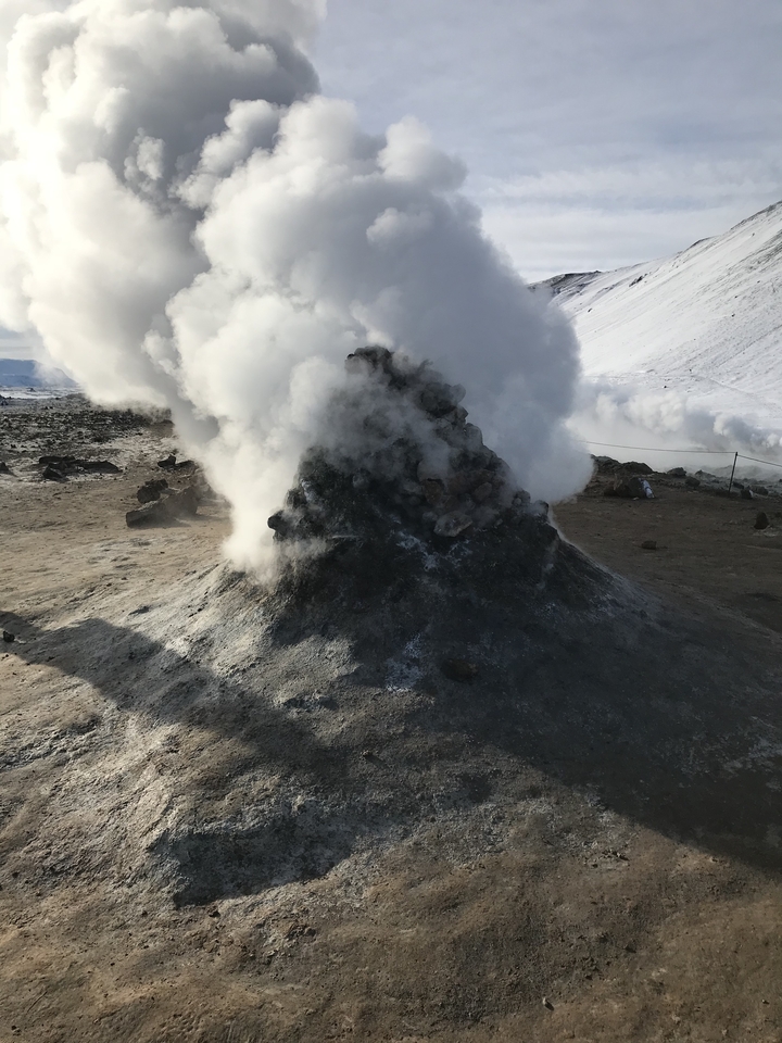 Une source géothermique fumante entourée d'un terrain rocheux et de neige en Islande.