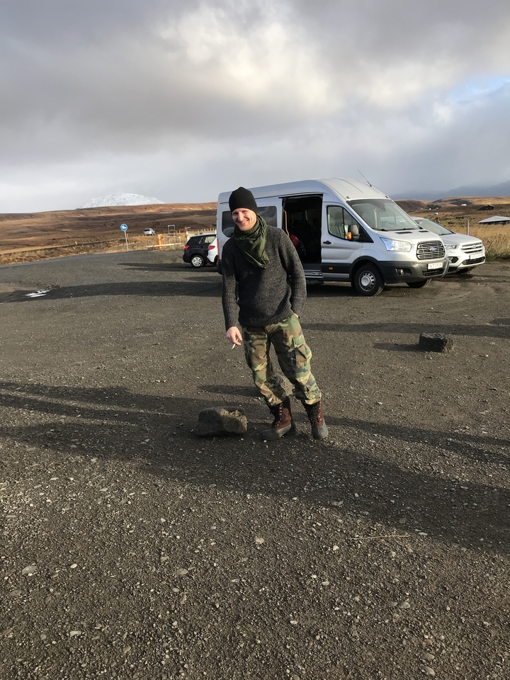 Homme debout près de véhicules garés sur une route de gravier.