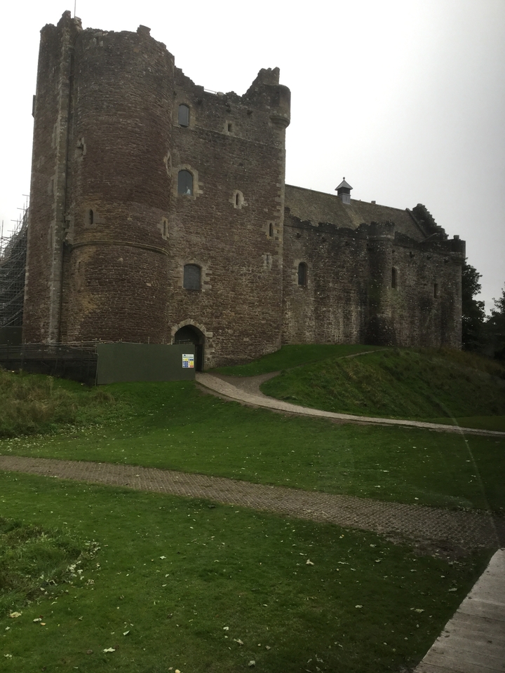 Un vieux château de pierre avec de l'herbe verte et un ciel nuageux.