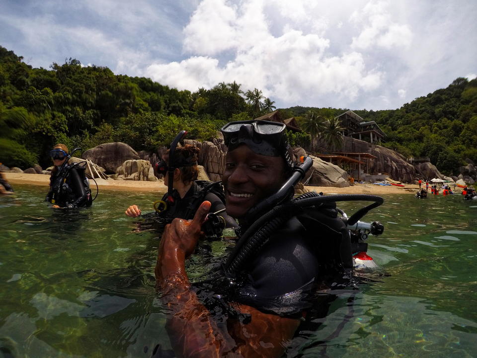 A person in scuba gear giving a thumbs up in the water near a beach.