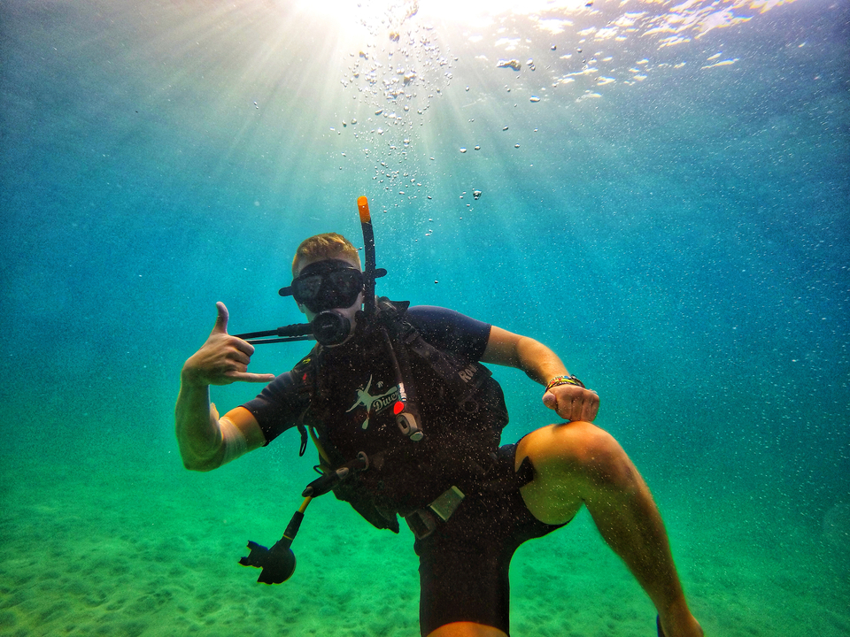 A diver making a hand gesture underwater with a bright light above.