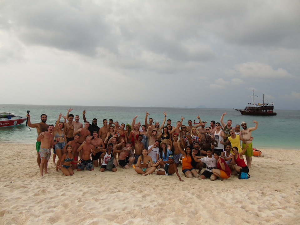 A large group of people on a beach with a ship visible in the background.